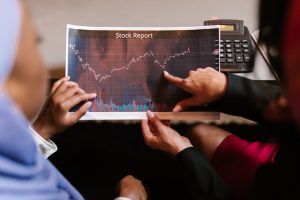 Two professionals discuss a stock report chart in a business meeting, analyzing data trends.